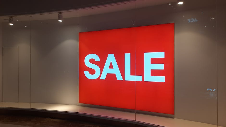 In the foreground, large, colorful cut-out letters spell the word 'SALE' on a dark surface, with each letter in a bright, distinct color: yellow for 'S', red for 'A', pink for 'L', and blue for 'E'. A